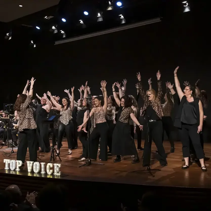 Las cantantes de Top Voice en concierto, con los brazos en alto sobre el escenario
